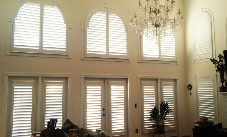 TV room in open concept Fort Myers home with plantation shutters on tall windows.