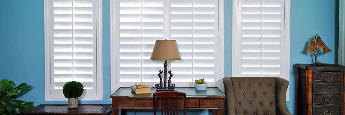 Interior window shutter in classic white behind wood furnishings and upholstered chair