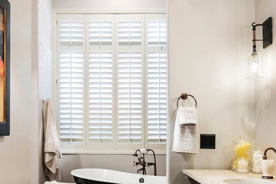 Insulate your bathroom with durable Polywood shutters. Large window with white Polywood shutters above a bathtub.