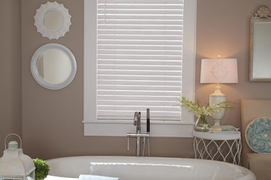 Enjoy the benefit of having moisture-resistant Polywood shutters on your bathroom windows. White and blue modern bathroom with two white Polywood shutter windows above a bathtub.