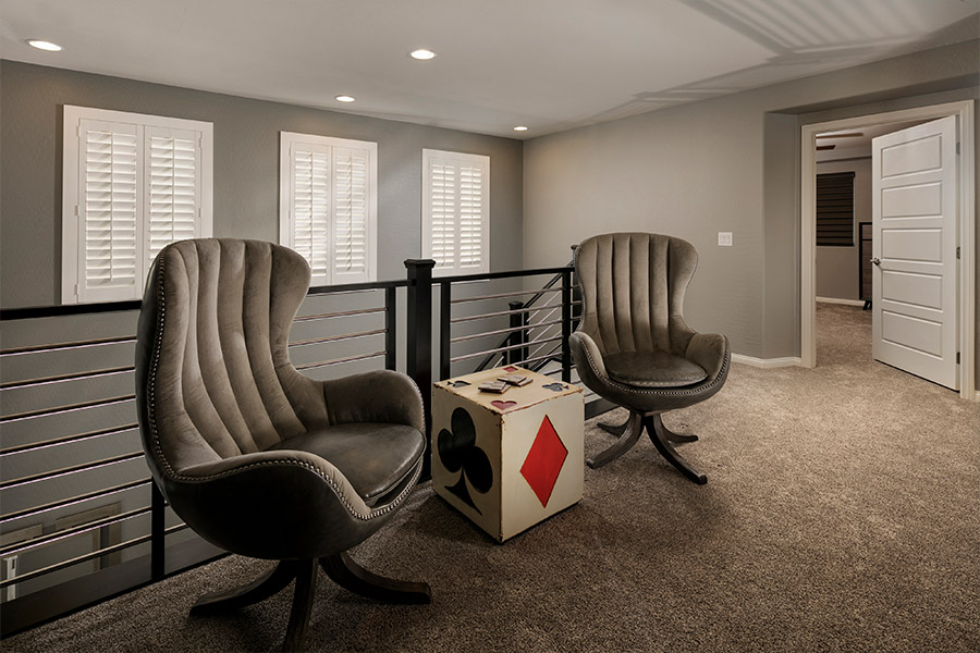 two chairs and a small dice-themed table in front of a stairwell with shuttered covered small windows