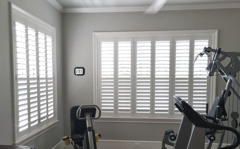 Draft-blocking window treatments are especially important in rooms with windows on more than one wall. Fort Myers home gym with shuttered windows.